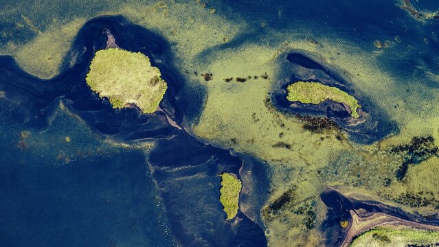 Aerial view of Hlidarvatn lake with its small green islands and dark blue water patterns in Sveitarfelagid Olfus, Iceland.