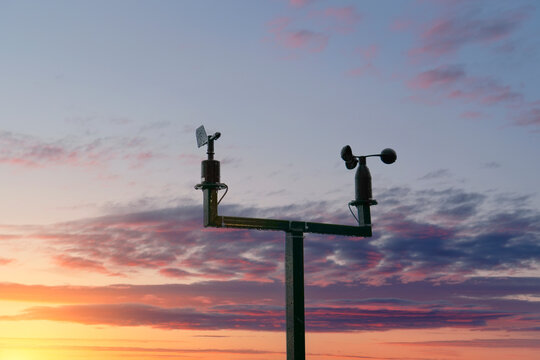A weather station stands tall as the sun sets, casting warm hues across the sky, creating a stunning backdrop of colors and clouds.