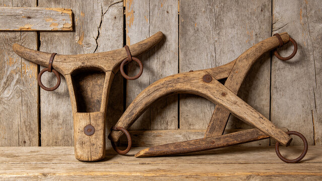 Two old wooden ox yokes with rusted iron rings against plank wall, agricultural heritage concept