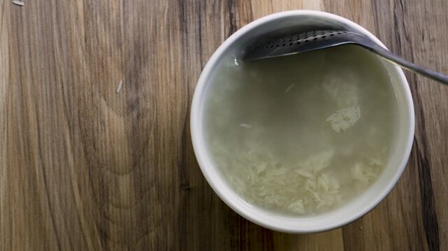 Stirring white basmati rice with spoon in water bowl top view, 4K