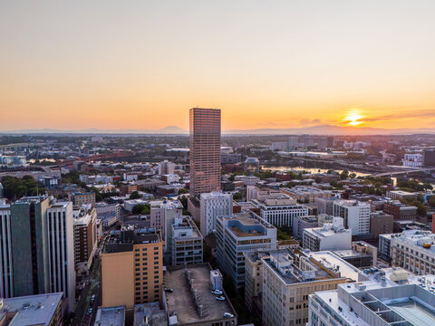 Aerial view of the Portland skyline at sunrise, featuring the Wells Fargo Center, surrounding urban buildings, and distant mountains under a warm golden sky in Portland, Oregon, United States.