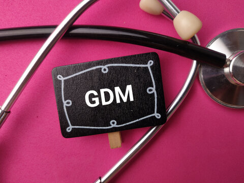 A small black chalkboard sign displaying GDM rests inside a stethoscope on a bright pink background