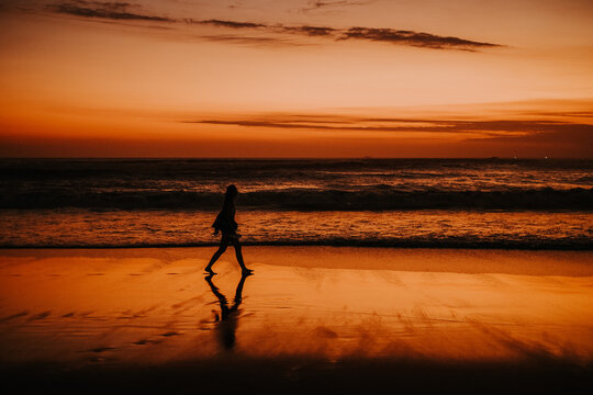 Majestic seascape setting the sky ablaze as a silhouetted person walks along the shore