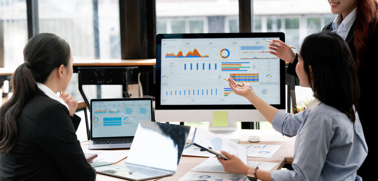 Asian Business Team Pointing at Computer Screen Analyzing Financial Dashboard in Office