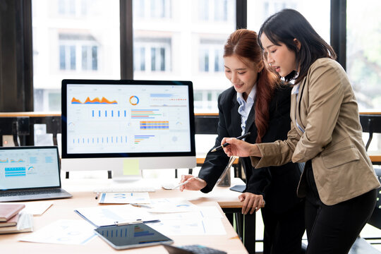 Asian Business Women Pointing and Analyzing Financial Charts on Computer in Office