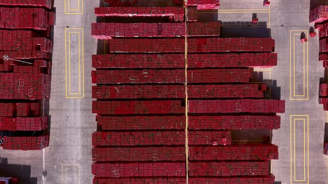 Overhead view of massive red beverage crate stacks arranged in rows on a marked concrete distribution center yard with yellow painted lines