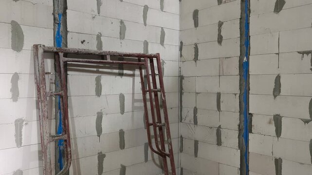 Autoclaved aerated concrete AAC block wall installation on a construction site. Features metal stiffeners and lintels for structural efficiency. Modern masonry techniques speed up building progress.