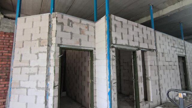 Autoclaved aerated concrete AAC block wall installation on a construction site. Features metal stiffeners and lintels for structural efficiency. Modern masonry techniques speed up building progress.