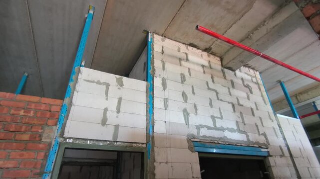 Autoclaved aerated concrete AAC block wall installation on a construction site. Features metal stiffeners and lintels for structural efficiency. Modern masonry techniques speed up building progress.