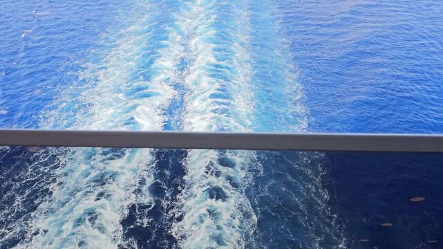 Sunlit wake trails behind a cruise ship as the camera tilts up at the stern