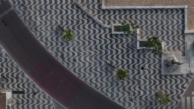 Aerial view of the iconic wavy cobblestone pavement at Praia da Ribeira de Cascais with palm trees and a statue in Cascais, Lisboa, Portugal.