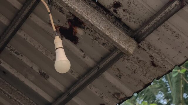 Close up of an old dusty light bulb turning on and then off in a dark ceiling
