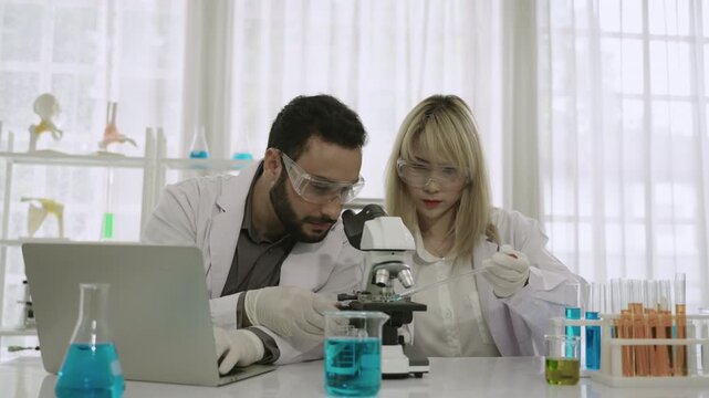 Two professional scientists and researchers are excited and happy about their success in conducting chemistry experiments on a medical vaccine, using a microscope and laptop in the science laboratory.