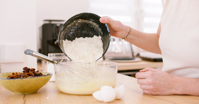 Kitchen work. Pouring flour. Woman confectioner hand adding ingredient in dough bowl kneading whisk tasty home treat with raisins eggs.