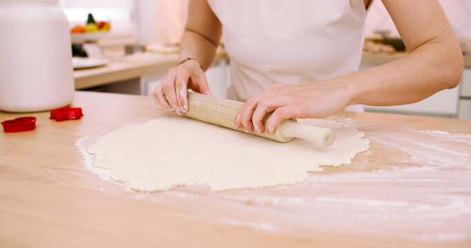 Homemade pastry. Treat recipe. Female confectioner hand rolling dough sheet with kitchen pin on flour countertop preparing cookies.