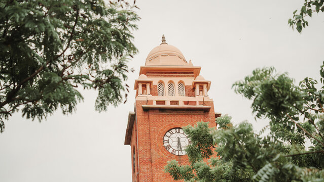 Historic red brick clock tower framed by green trees