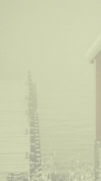 A person stands on a wooden dock looking over the water. Fog surrounds the area making it difficult to see. Fishing gear lies on the dock while nature appears quiet.