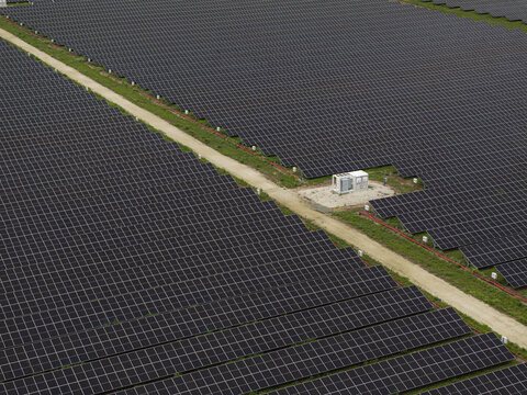 Aerial view of a large solar farm with rows of photovoltaic panels, a dirt access path, and an electrical inverter station in Miami, Florida, United States.