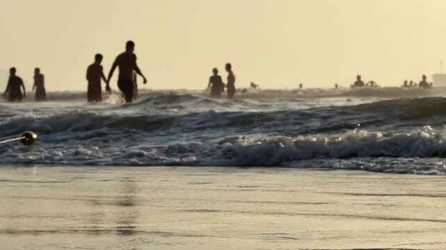 Close up of Beach Buoy on Rope at sandy Shoreline and people silhouettes in the water in background