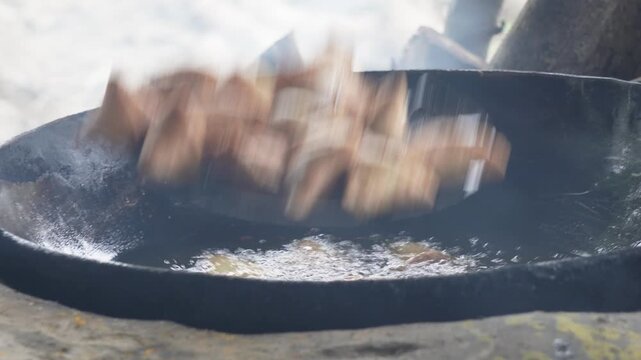 Samosas deep frying in hot oil over outdoor stove