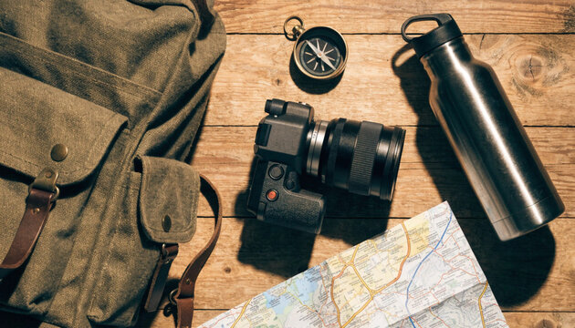 Travel adventure gear flat lay with backpack compass camera and map on wooden floor
