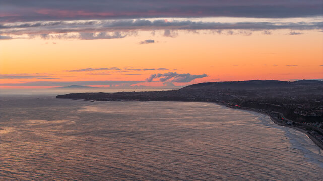 Aerial view of the coastline at sunset with calm ocean waters, rolling hills, and a vibrant orange sky over San Clemente, California, United States.