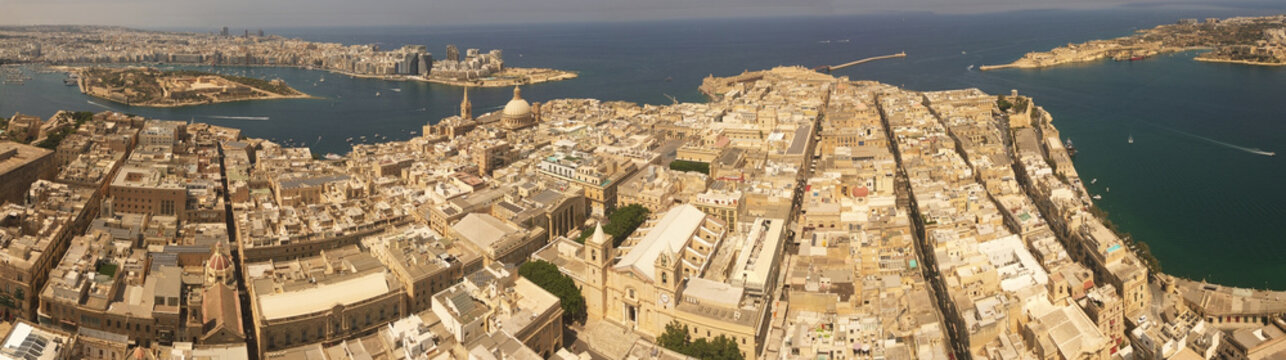 Aerial view of the historic city of Valletta featuring dense limestone architecture, the iconic dome of the Basilica of Our Lady of Mount Carmel, and the harbor in Valletta, Port Region, Malta.