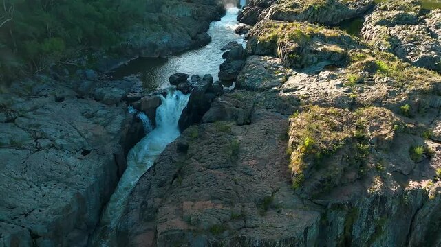 Aerial view of Barron Falls with cascading water flowing over rugged rock formations and lush tropical vegetation in Kuranda, Queensland, Australia.