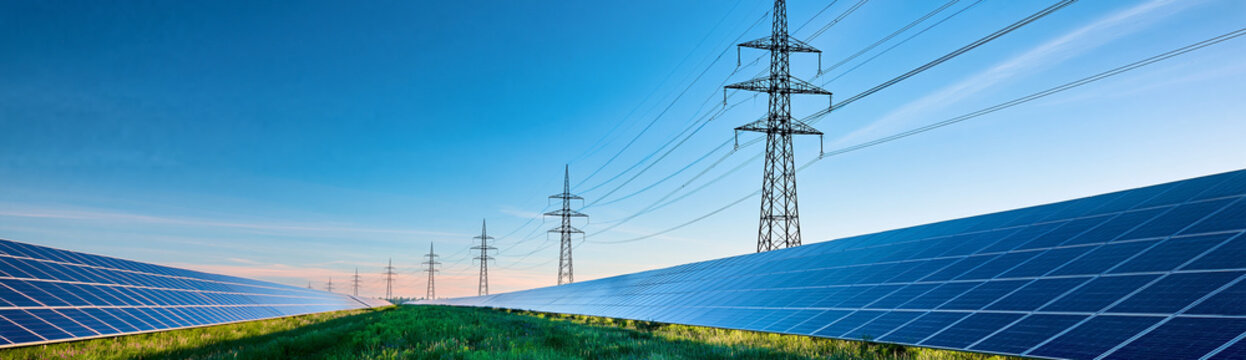 Solar panels and power lines stretch across a green field under a clear blue sky, symbolizing renewable energy and sustainable power generation.