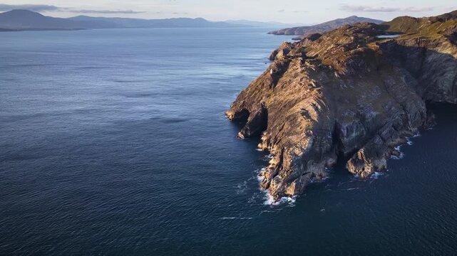 Aerial footage of rugged rocky cliffs, covered in sparse coastal vegetation, stretching out into waters of Atlantic Ocean. Aerial view of rugged cliffs, coastline at Sheep's Head Peninsula, Ireland