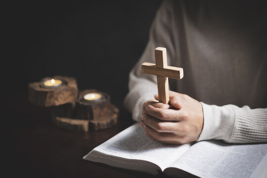 A Christian woman praying beside a cross in a quiet room, expressing faith, hope, devotion, peace, and trust in God.