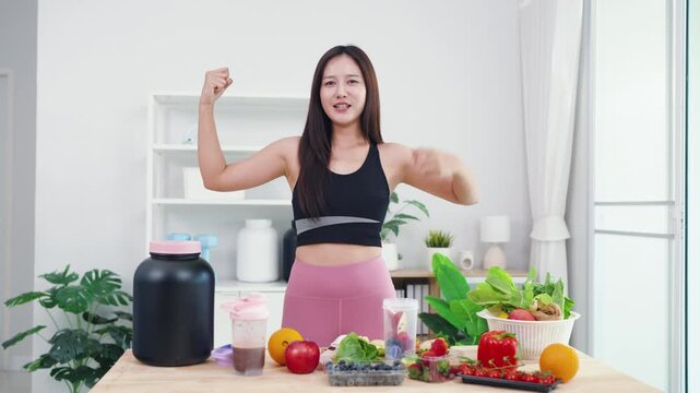 Energetic young female live streaming plant-based diet tutorial using smartphone. Asian wellness vlogger showing fresh vegetables for healthy sports nutrition and vitality.