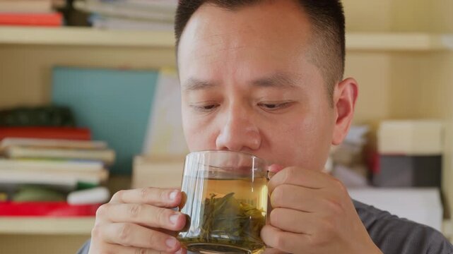 Vertical Video: Asian man blows hot tea to cool down before drinking to avoid burning mouth.