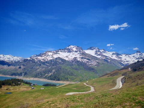 Panoramic view of Roselend Lake with snowy Alpine peaks, green hills, hiking trails and evergreen forest, haking 