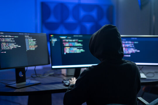 Hacker male wearing hoodie typing on computer keyboard in dark room, Concept of cybersecurity, cybercrime, software engineering, dark web, data breaches and modern digital network protection