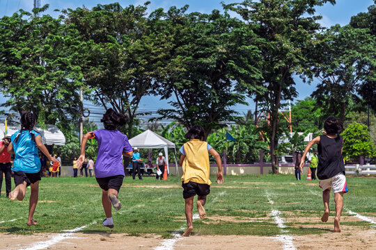 Schoolgirls sprinting toward finish line at sports day. Back view of young schoolgirls competing in running race on grass and dirt field track, sprinting towards finish line during school sports day