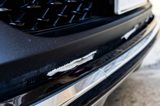 Front bumper show torn, detached, peeling and broken lower rubber skirt lip or trim beneath under grille. Vehicle wear and tear,  Damaged front bumper and torn rubber lip of car. Loss of adhesion.