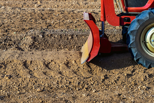 Agricultural tractor standing with front blade and rear rotary tiller on tilled agricultural field during land preparation for farming with trees and cornfield in background. Agricultural machinery.
