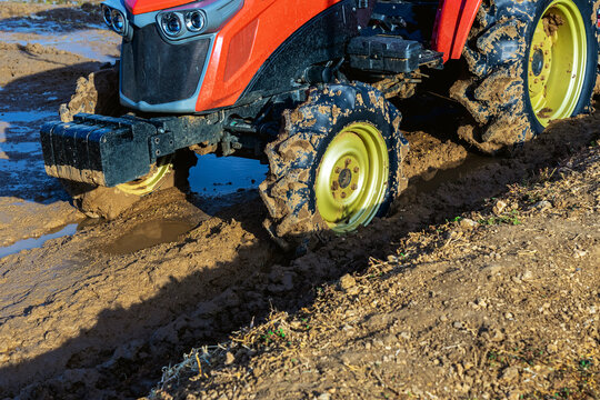 Agricultural tractor standing with front blade and rear rotary tiller on tilled agricultural field during land preparation for farming with trees and cornfield in background. Agricultural machinery.