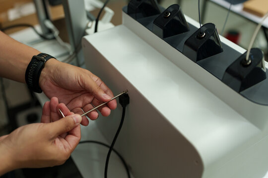 The focus is on the hands of a technician setting up a 3D printer to print a clear white plastic model, using cutting-edge technology and concentrating on specific points within the laboratory.