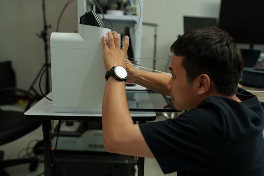 The focus is on the hands of a technician setting up a 3D printer to print a clear white plastic model, using cutting-edge technology and concentrating on specific points within the laboratory.