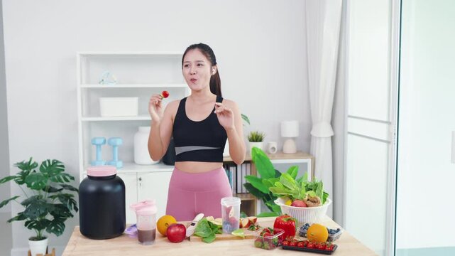 Energetic young female live streaming plant-based diet tutorial using smartphone. Asian wellness vlogger showing fresh vegetables for healthy sports nutrition and vitality.