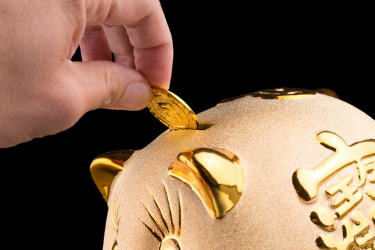 Hand Putting Coin into Gold Piggy Bank on Black Background