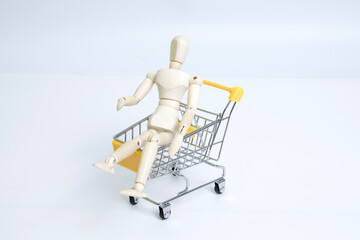 Wooden mannequin sitting in miniature shopping cart on white background © PhamHong