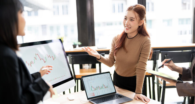 Asian Business Team Gesturing and Analyzing Stock Market Candlestick Charts in Office