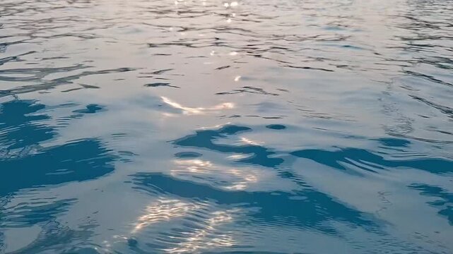 Close-up of calm blue swimming pool water with sparkling golden sunlight reflections and gentle waves.