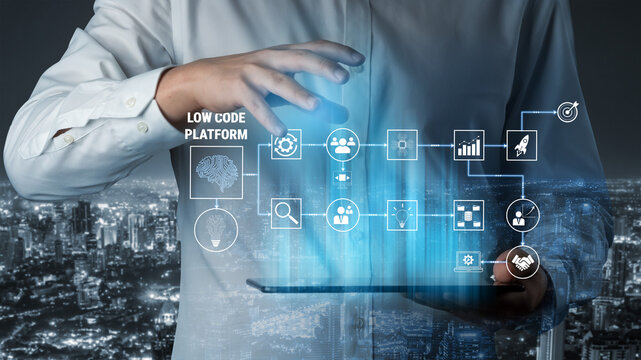 Low Code Platform Concept With Businessman Using Digital Tablet Over Skyscraper Cityscape At Night With Transparent Icons And Symbols Quark.