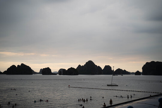 Scenic view of rocky islands under a cloudy sky with swimmers in the foreground.