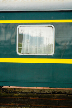 Green train carriage with a window draped in a sheer curtain.