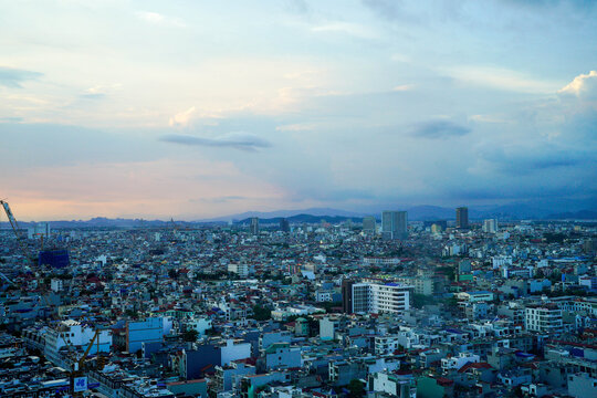 Aerial view of a bustling cityscape during twilight, featuring urban buildings and distant mountains.